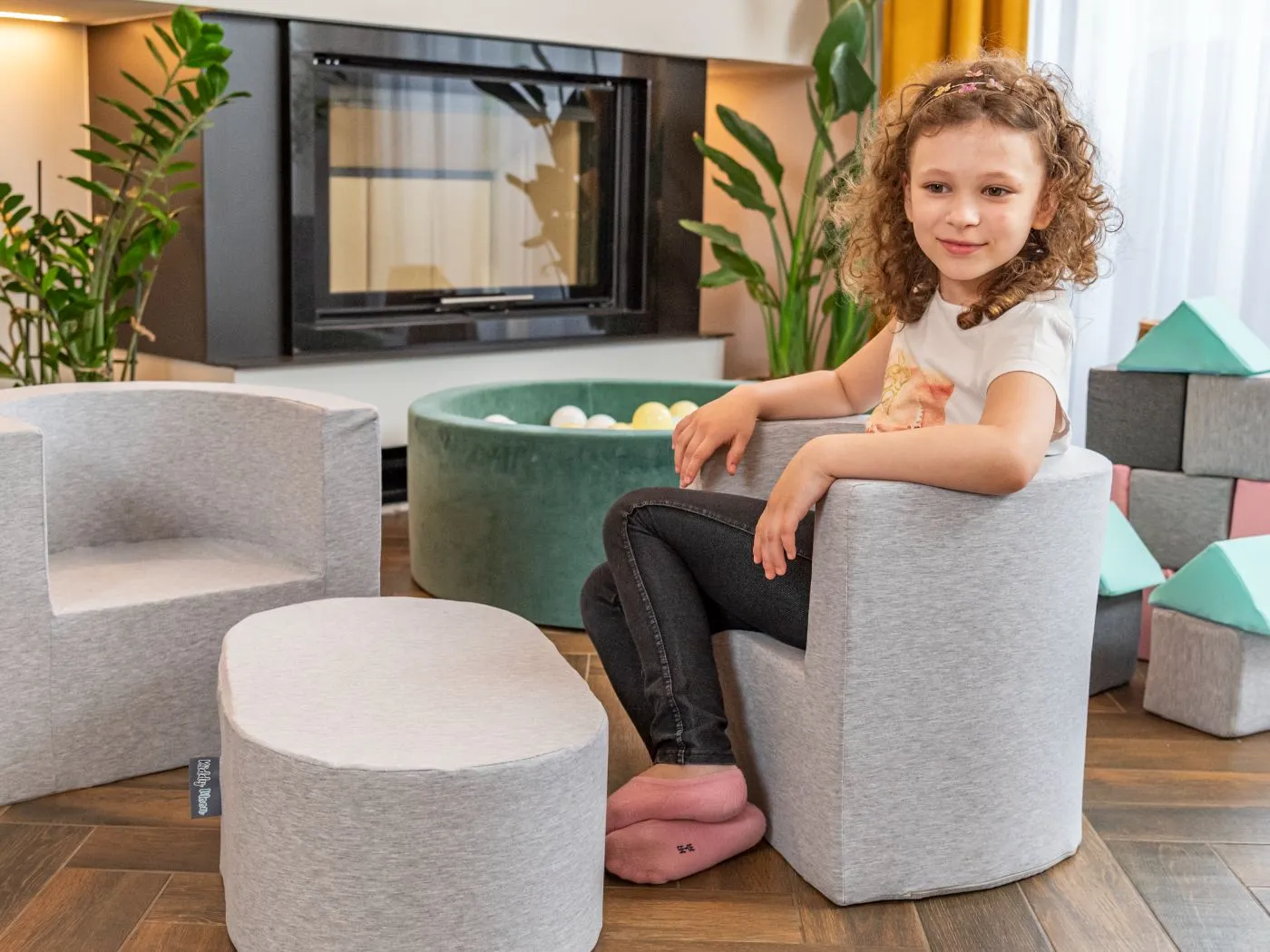 Mädchen sitzt auf einem grauen Schaumstoff-Sessel mit passendem Hocker im Wohnzimmer